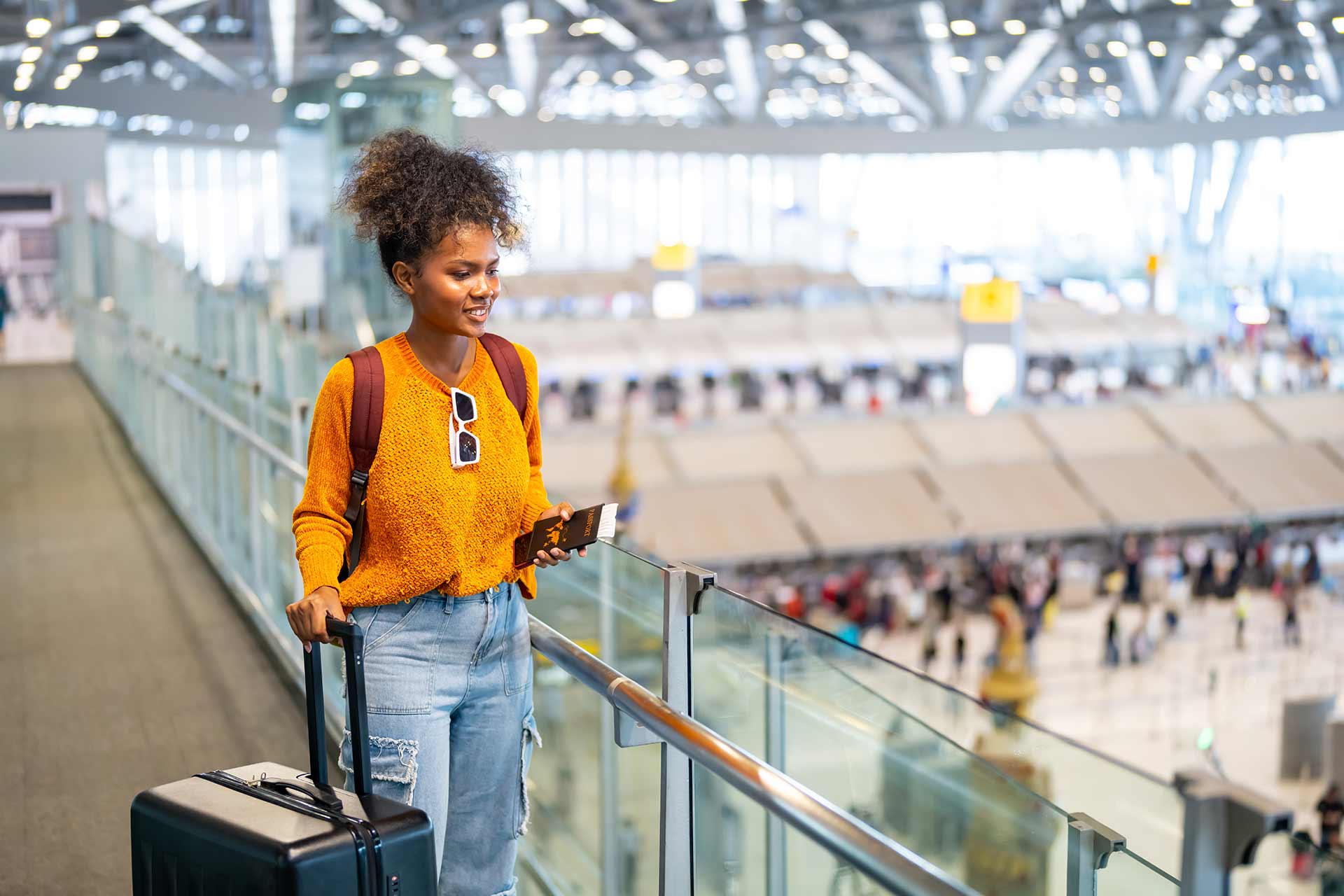 A student wheels a suitcase along a walkway at an airport.