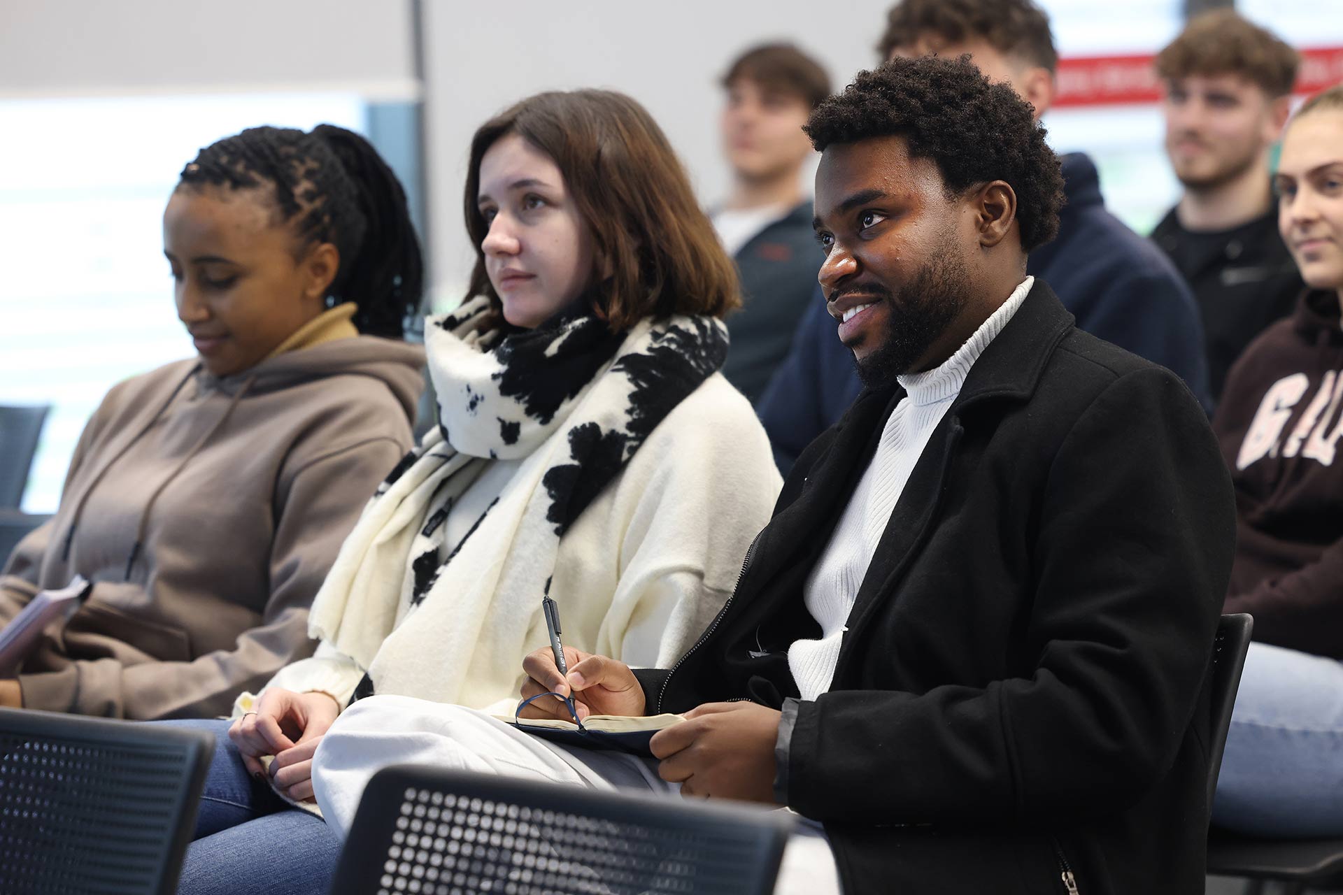 Three students sitting in a row of chairs listening to a lecture at the University of Liverpool