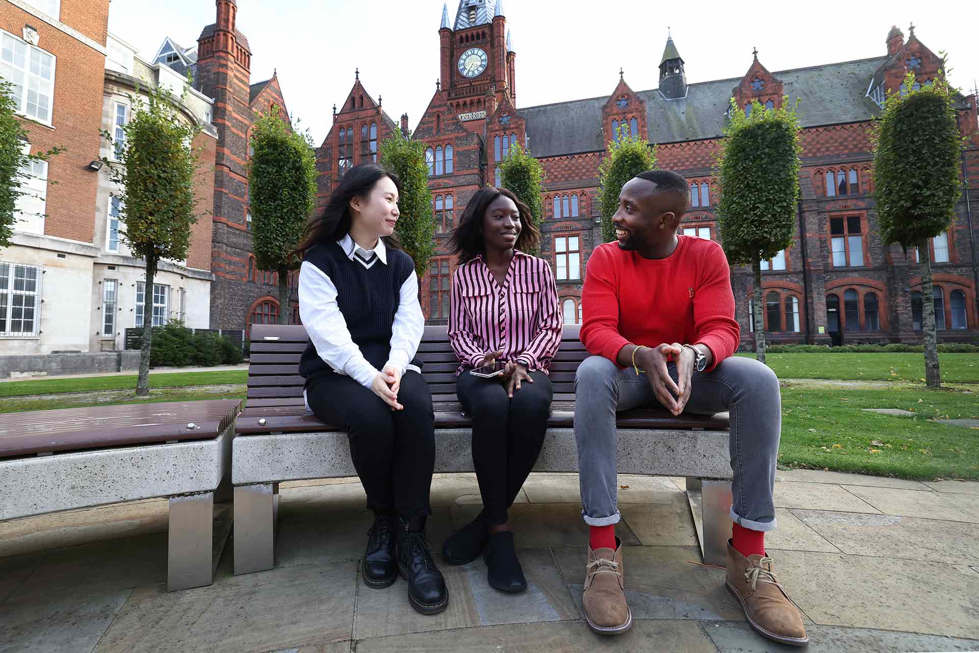 Three students chatting while sat on a bench in the Quad.