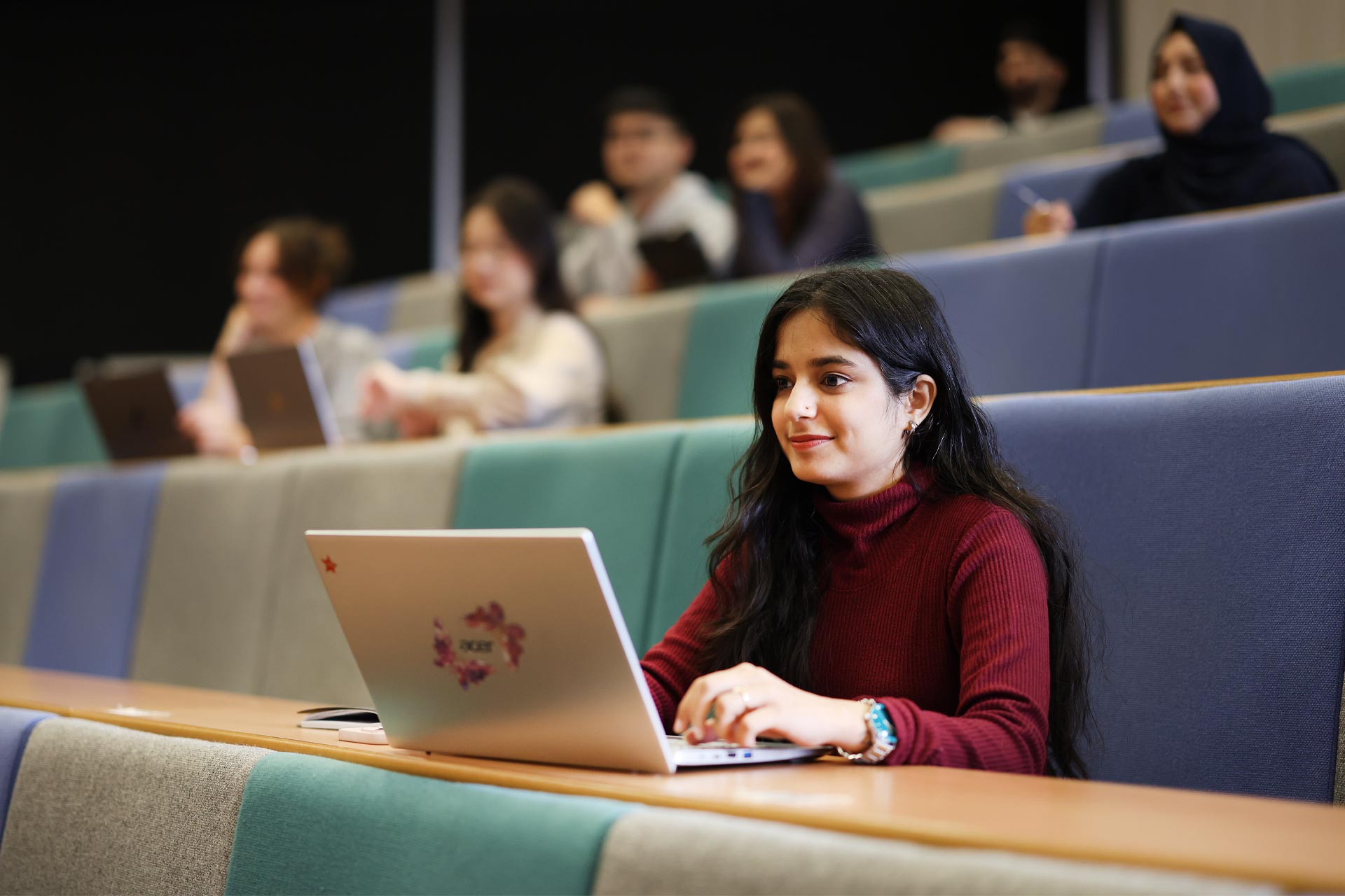 An international student sits at their laptop in a lecture theatre.