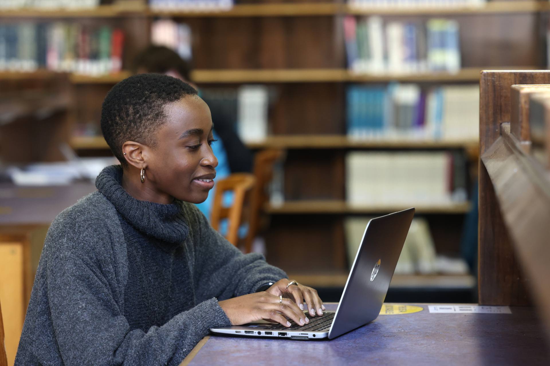 A student sitting at a desk in the library, working on a laptop.