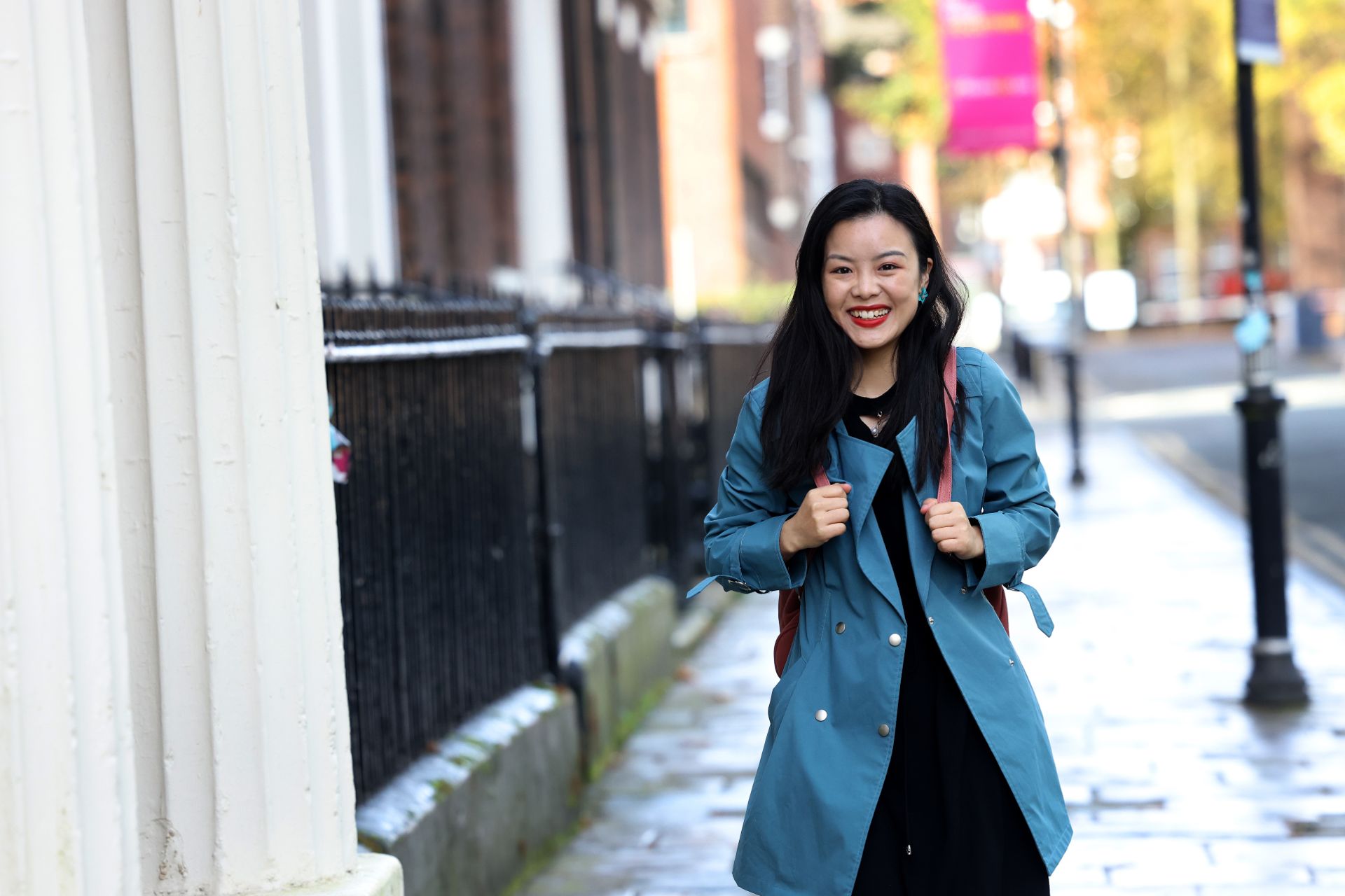 A student is walking through campus, smiling and carrying a backpack.