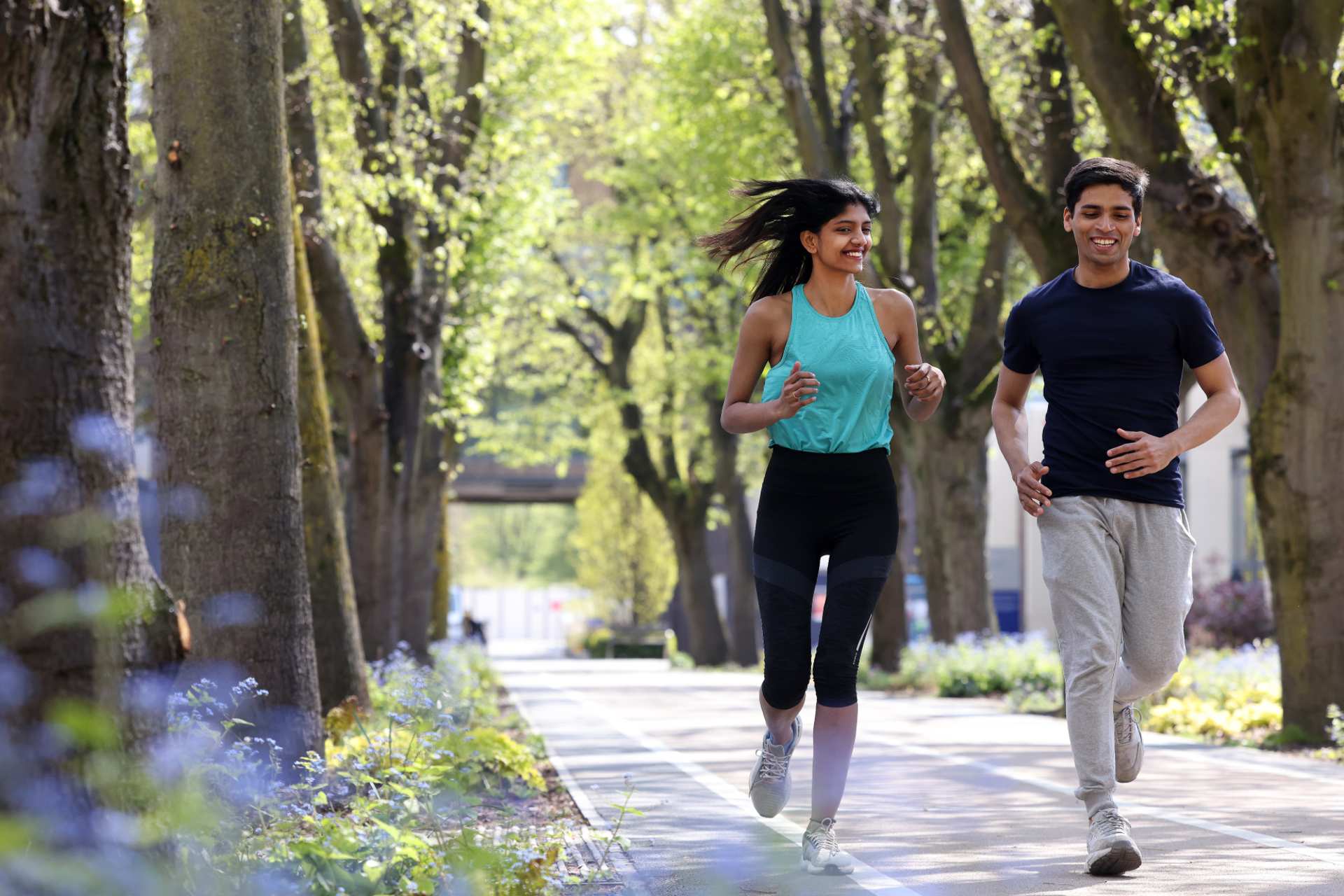Two students using the outdoor running track on campus on a sunny day.