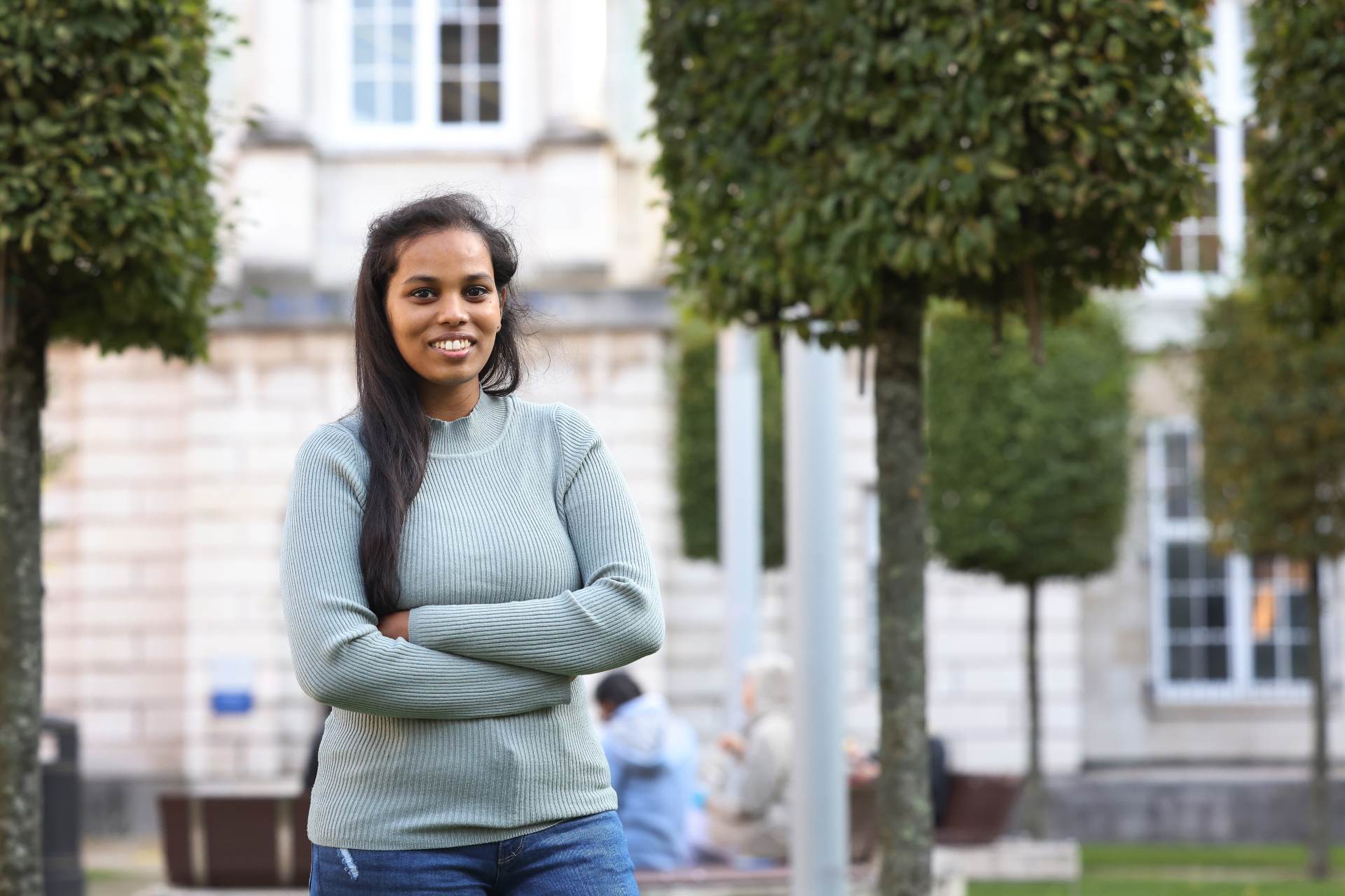 A student standing outside smiling at the Quadrangle.