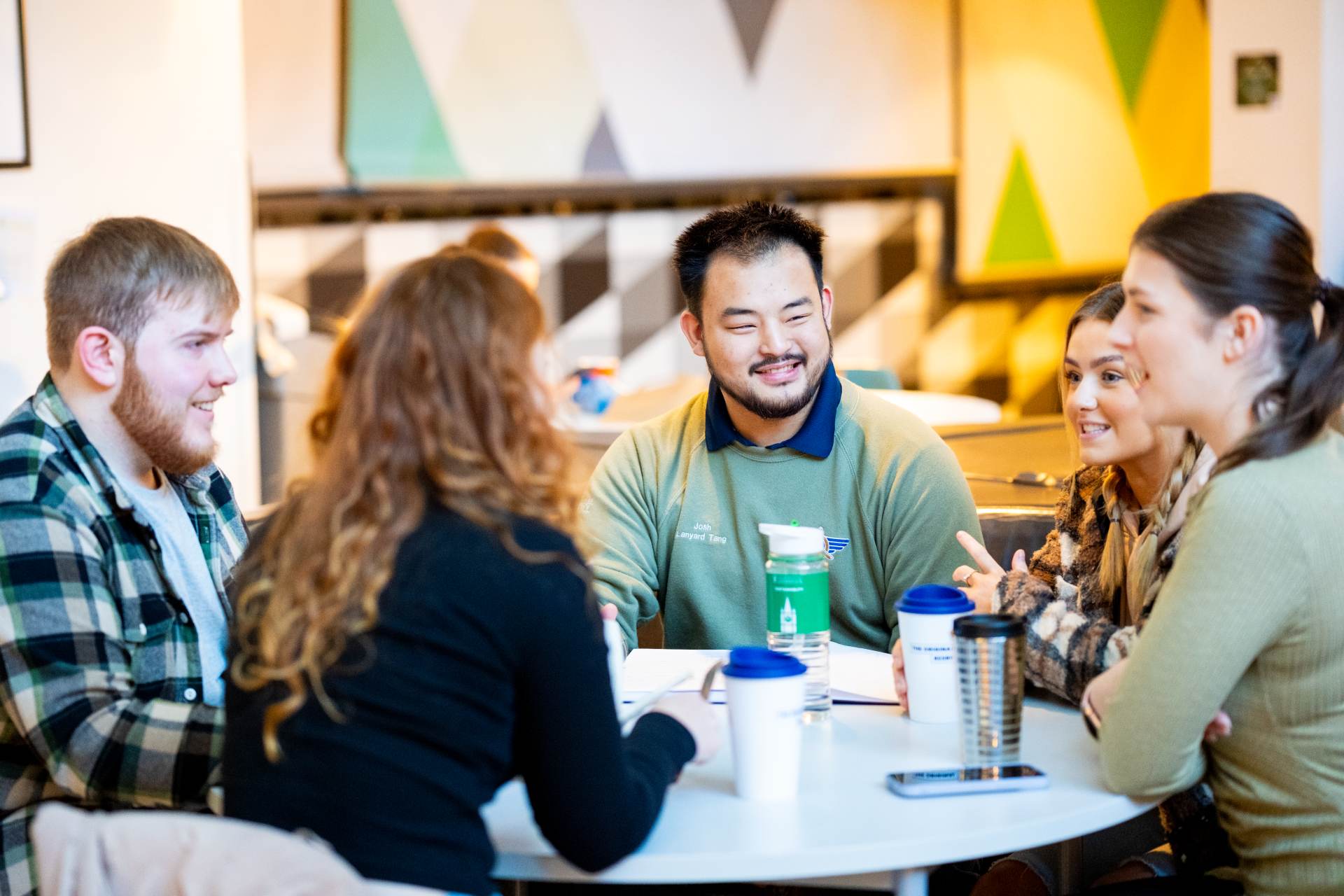 A group of students sitting around a table talking and drinking coffee.