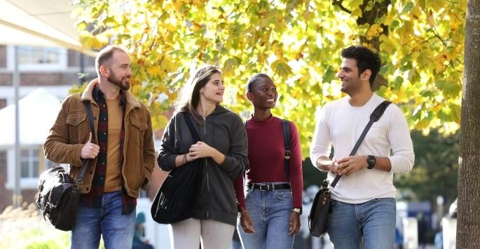 Four students walk on campus on a fall day, laughing and talking to each other.