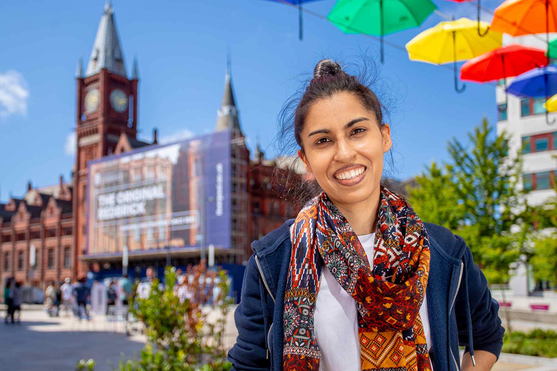 A PhD student standing under an art installation of umbrellas in University Square.