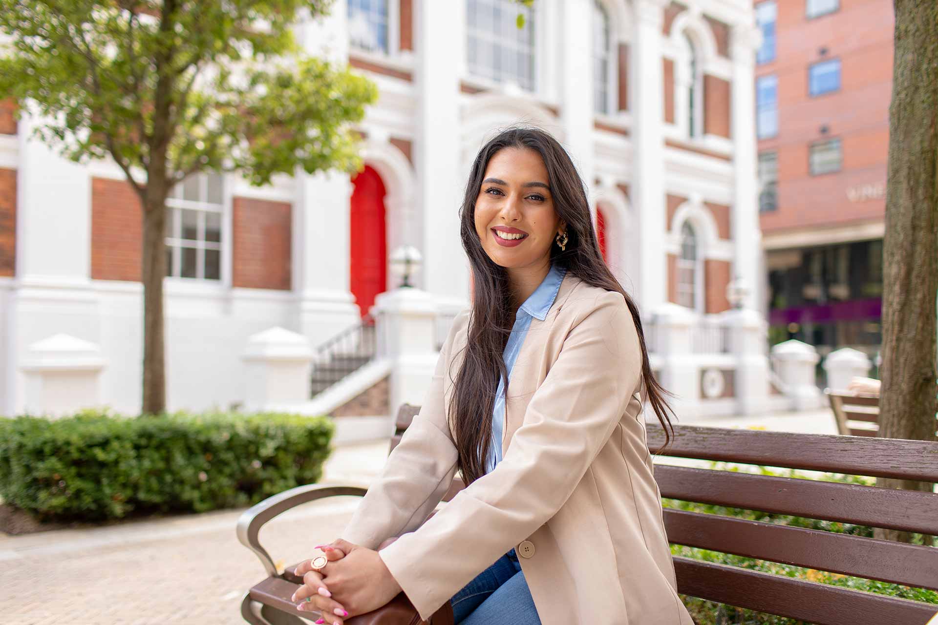 A postgraduate researcher sits on a bench outside the Management School.