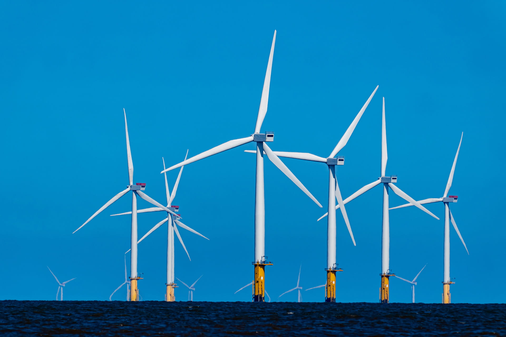 Wind turbines at sea against a bright blue sky