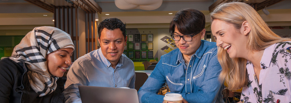 four students looking at a laptop and smiling