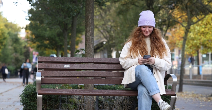 A student sitting on a bench using a phone.
