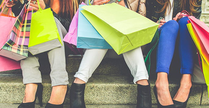 Photograph of the legs of three people who are sitting down and carrying lots of shopping bags