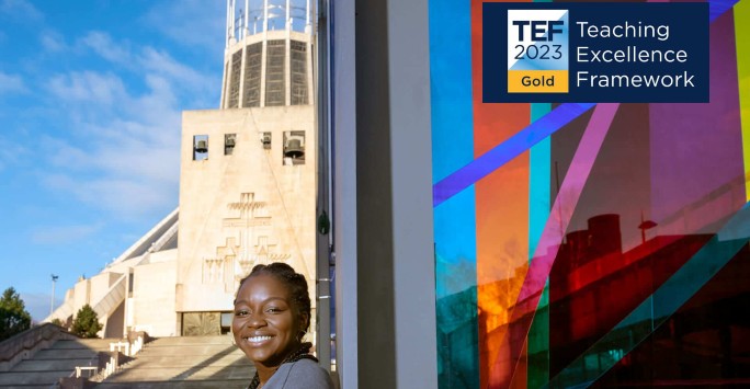 A student is smiling in front of Liverpool Metropolitan Cathedral. The logo for Teaching Excellence Framework Gold 2023 is displayed in the top right corner of the image.