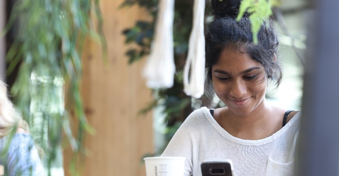 A student sitting at a table using their phone and smiling