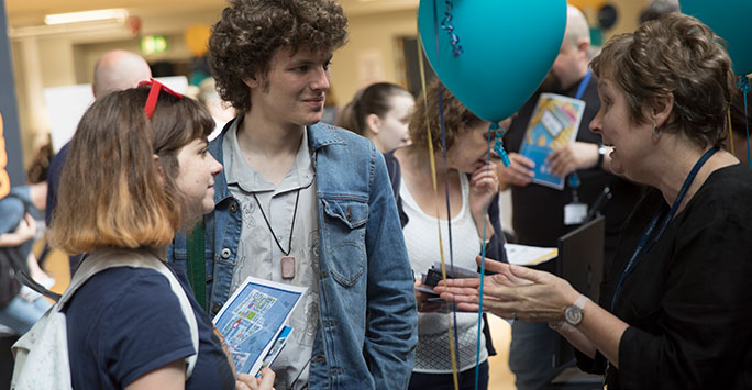 A University of Liverpool member of staff talking to two prospective students at a Higher Education fair.