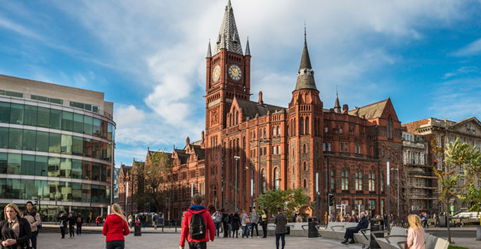 University square with students walking to lectures in the foreground, with the Foundation Building and Victoria Building in the background.