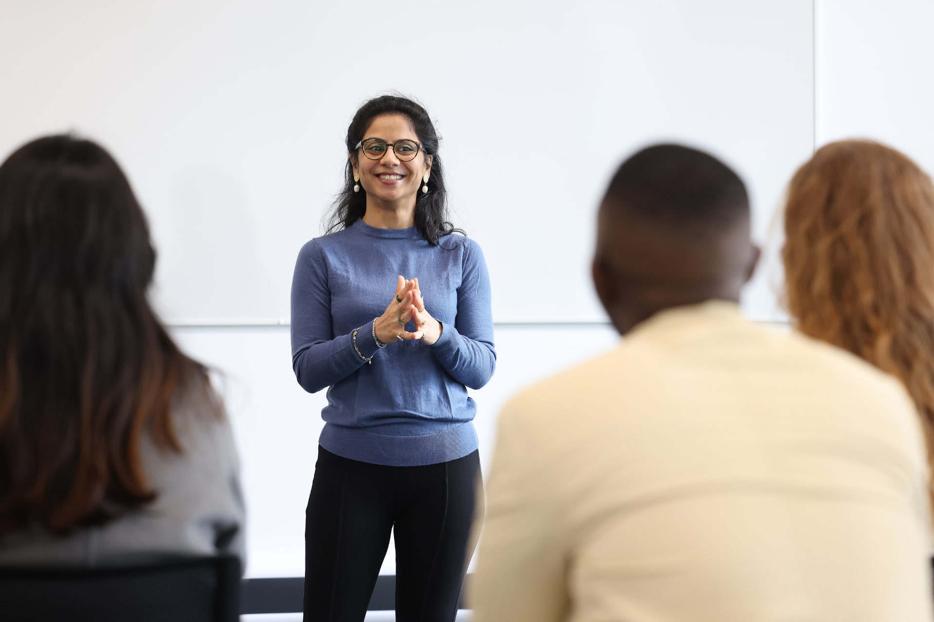 A teacher stands at the front of a classroom smiling.