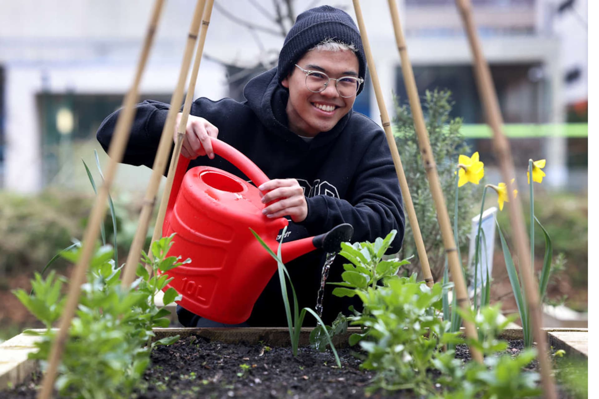 A smiling student watering plants with a red watering can.