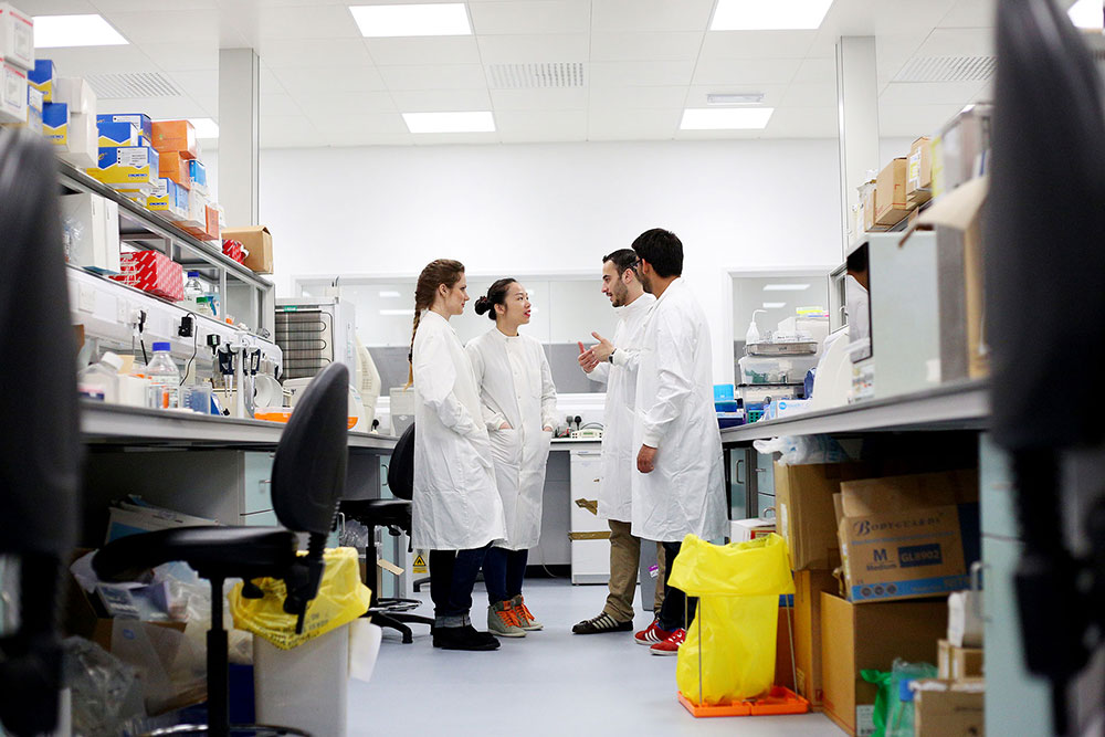 A group of students in white lab coats having a discussion in a lab