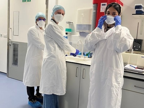 Jasmine Heenan in the lab in a lab coat and mask, alongside two researchers