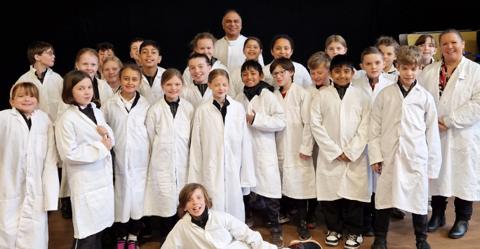 A group photo of school children in lab coats with Dr Muhammad Awais