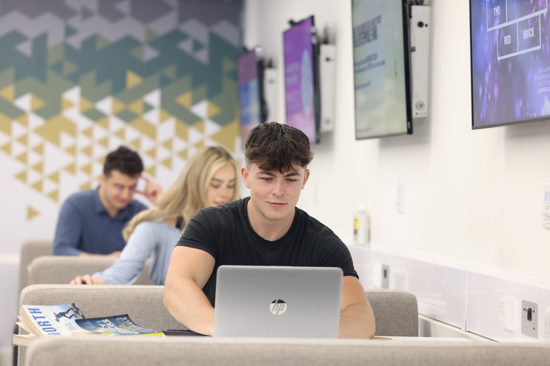 A student is sat at a booth working on a laptop.