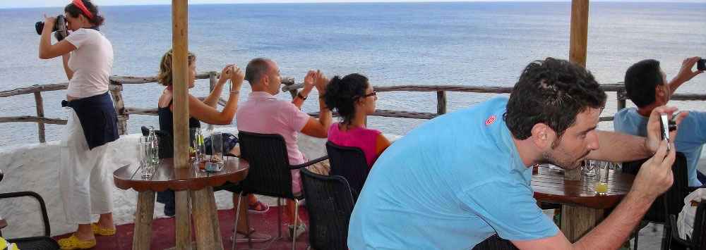 A group of tourists all on electronic devices taking a picture of the view rather than looking at it.