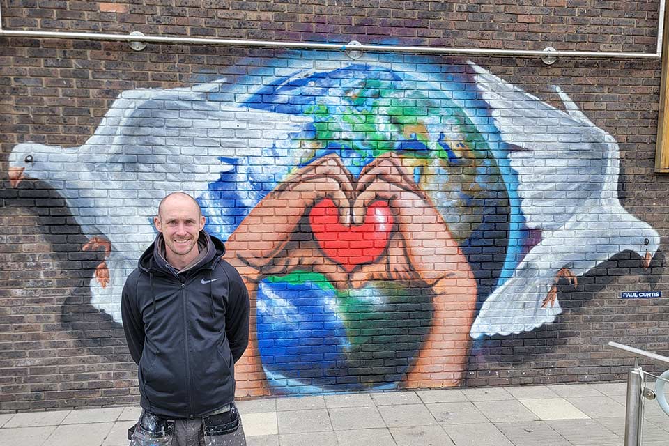 Paul Curtis standing in front of the mural he created on-campus