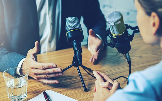 Two people talk into microphones.