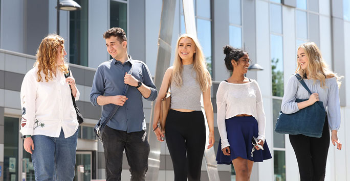 A group of 5 students walking on campus smiling and talking each other.