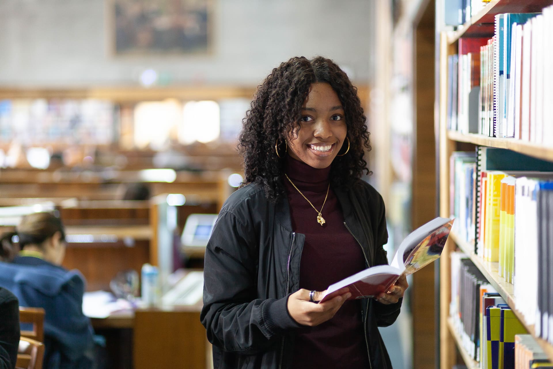 Student in library holding a book smiling at camera