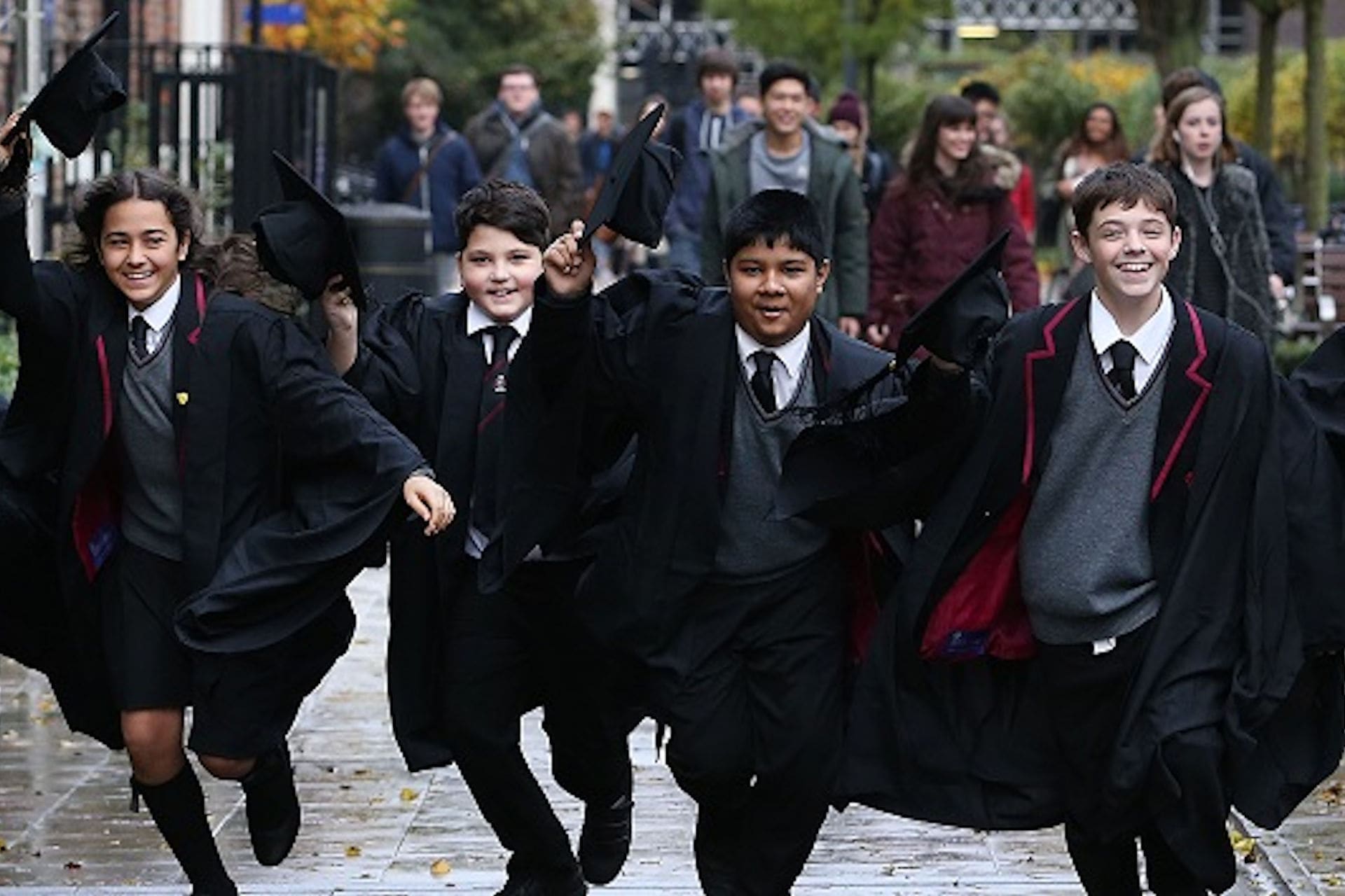 WP school students in cap and gown running towards camera smiling raising caps