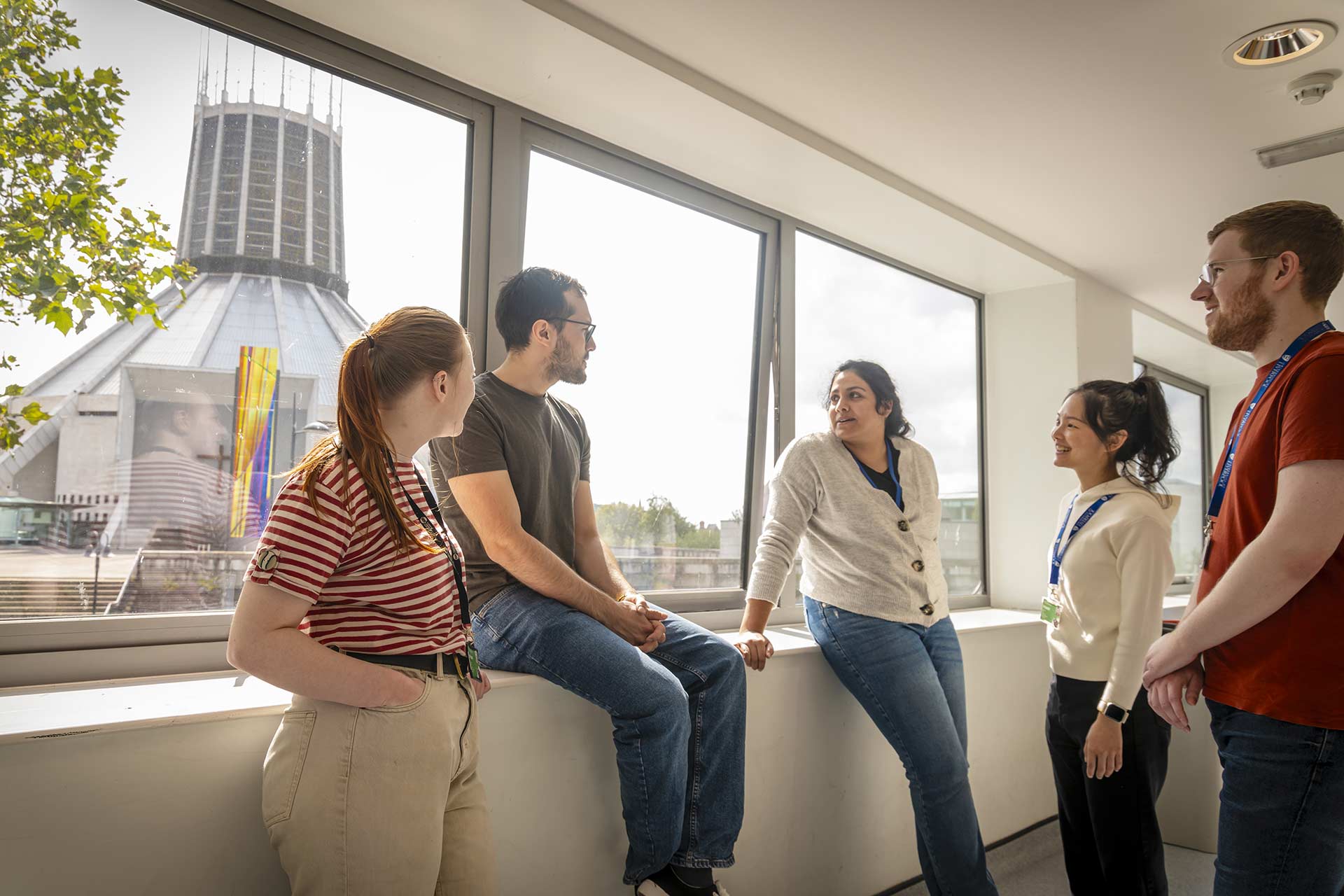 A group of students are gathered around a window, which faces out onto the Liverpool Metropolitan cathedral