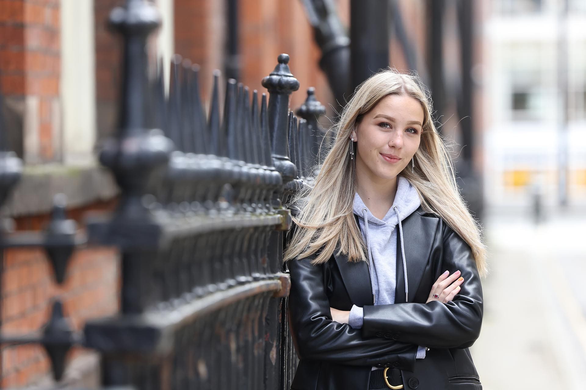 A student leans against a fence on the streets of Liverpool, ready to find a postgraduate programme that works for her.