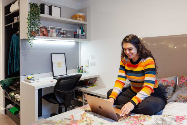 A student working on a Macbook while sat on a bed in a True Student Double Ensuite bedroom.
