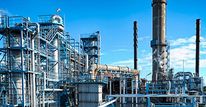 A large oil refinery featuring extensive networks of pipes and industrial structures against a clear sky.