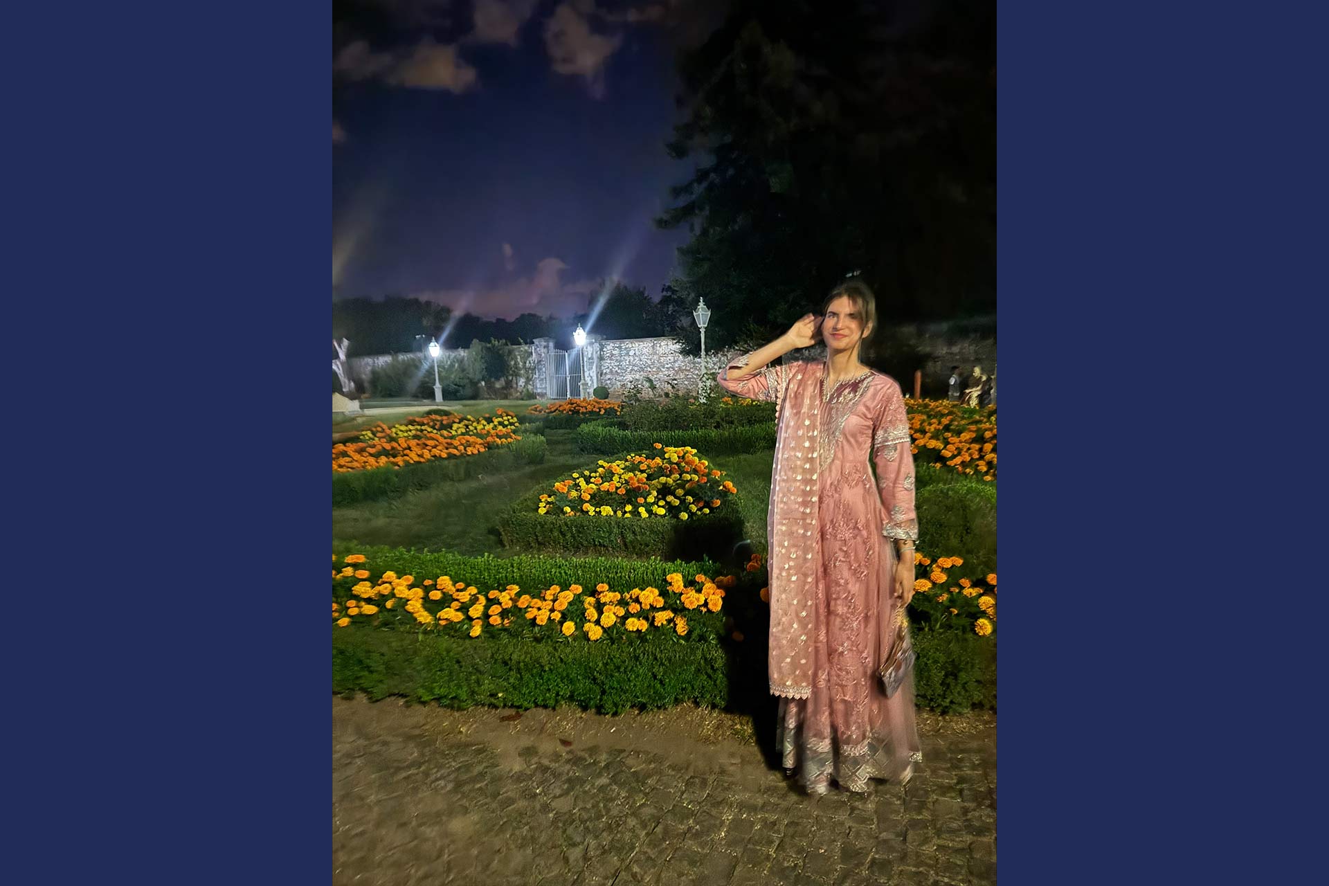 A woman with dark hair wearing a sari next to a bed of flowers
