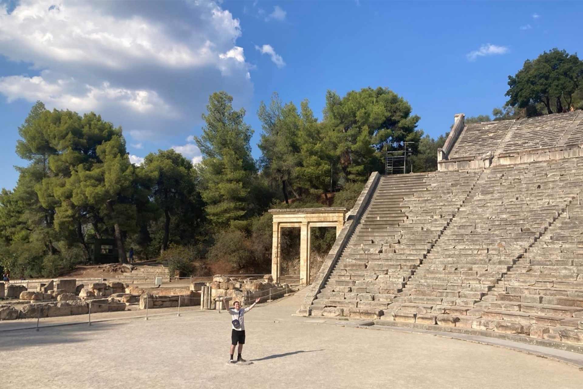 A man standing at a distance next to a large ancient structure in a sandy dry landscape.