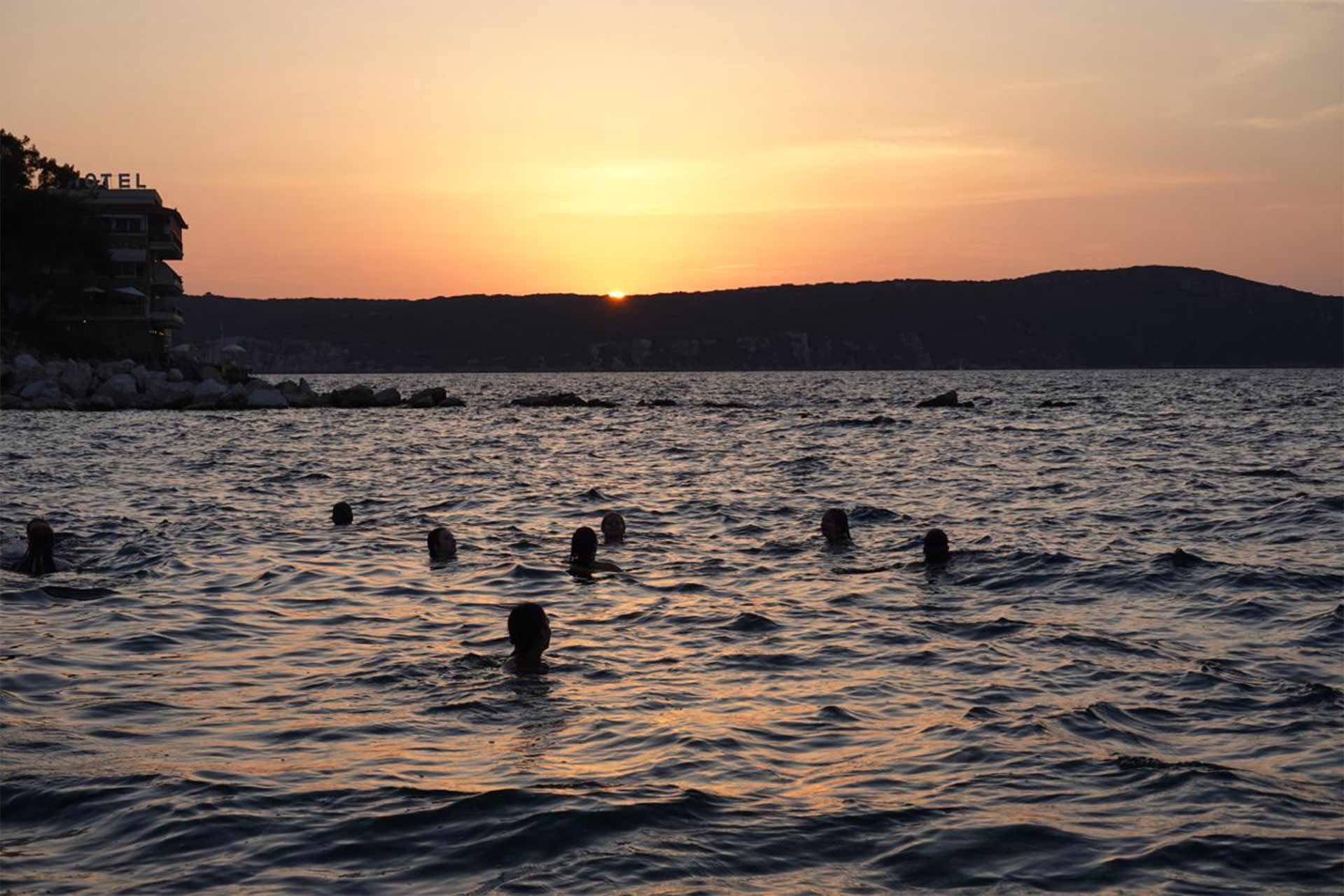 Sun setting on the shore, with people's heads bobbing in the water
