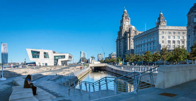 Person sitting alone by a canal in front of a canal, on the other side are several tall stone classical buildings.