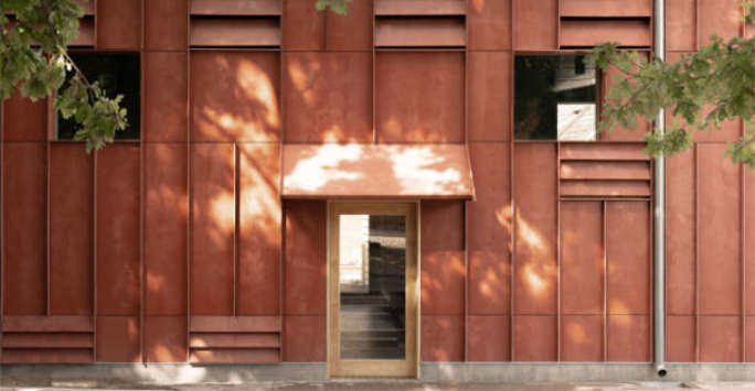 Rust coloured building with prominent vertical ribs and vents, framed by foliage