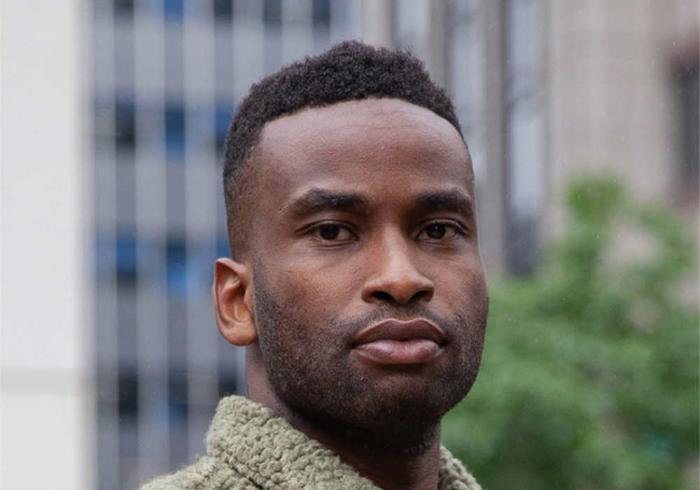 Young man with short cropped afro hair wearing a fluffy sage shirt.