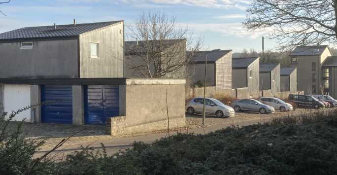 Row of two story urban houses with pitched roofs. A row of cars is parked in front.