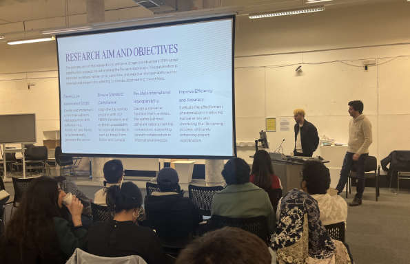 A man standing by a screen speaking. On the screen is a slide exploring naming conventions in BIM. A audience is in front listening.