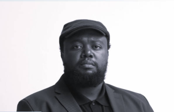 Beared black man wearing a suit jacket and buttoned up shirt.