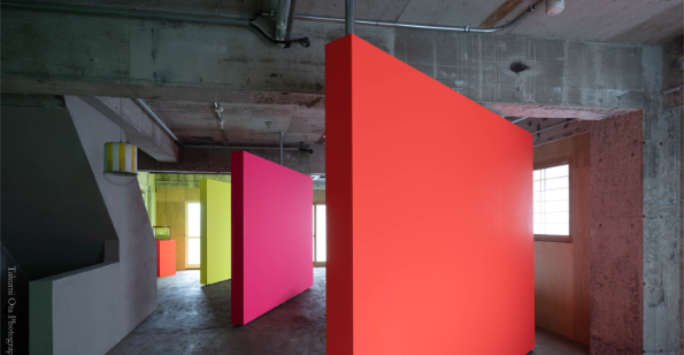 Large angled vertical rectangular panels in primary colours inside a concrete warehouse space.