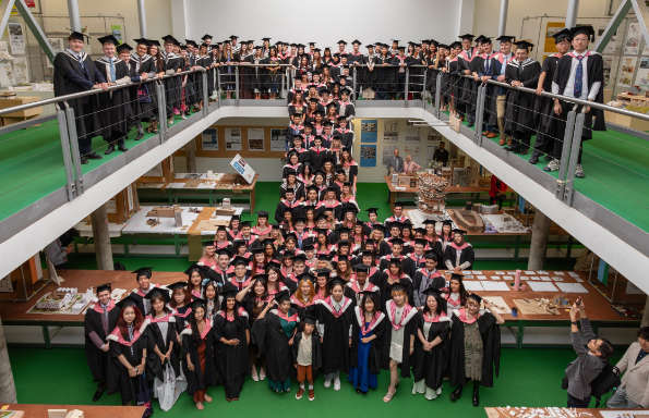 A crowd of graduate students on two levels with a number standing on a set of stairs in the middle.