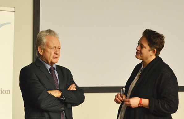 Woman and a man standing in front of projection screen, engaged in an intellectual conversation.