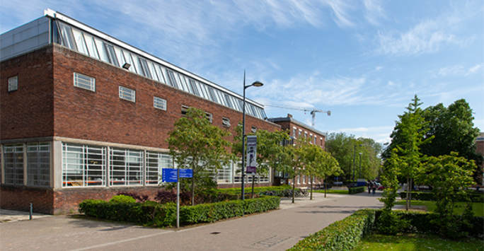 Brick built building with a H-Tech steel roof, fronted by a pavement, trees and a hedge.
