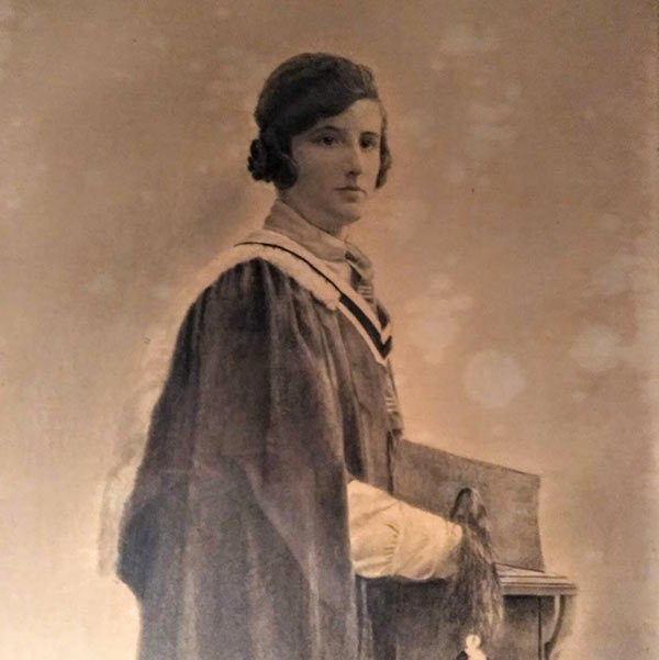 Sepia photograph of a woman wearing a formal graduation gown and holding hat